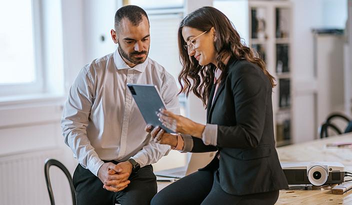 Deux collègues assis sur un bureau qui consultent une tablette 