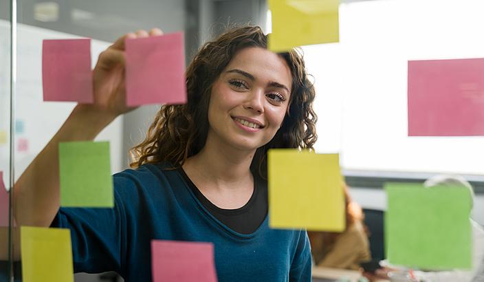 Jeune femme qui dépose des post-it sur une paroi en verre