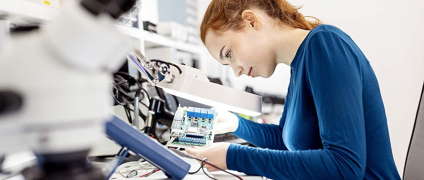 Jeune femme assise à son bureau qui vérifie un circuit électrique