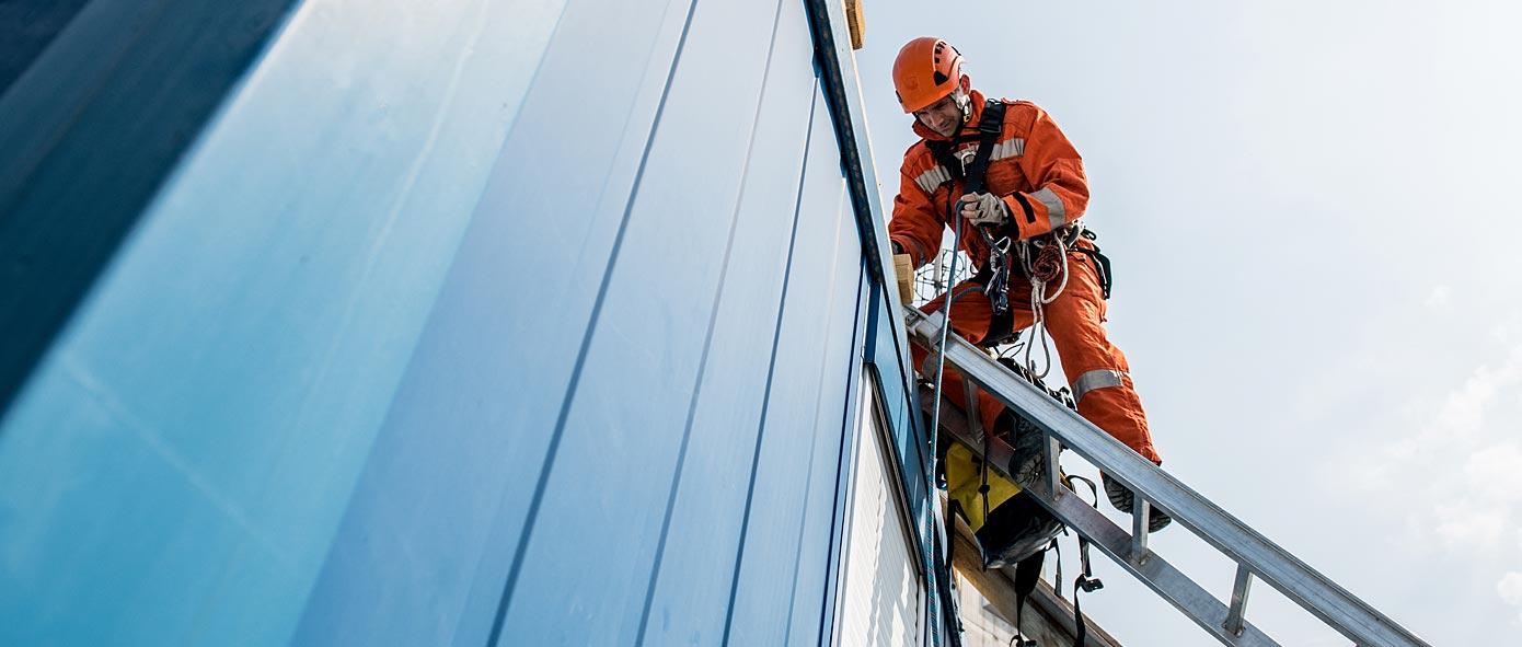 Homme sur une échelle appuyée sur une façade de bâtiment