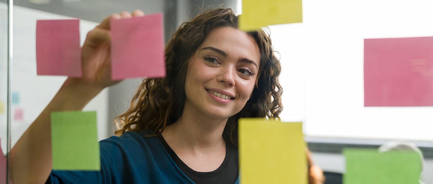 Jeune femme qui dépose des post-it sur une paroi en verre